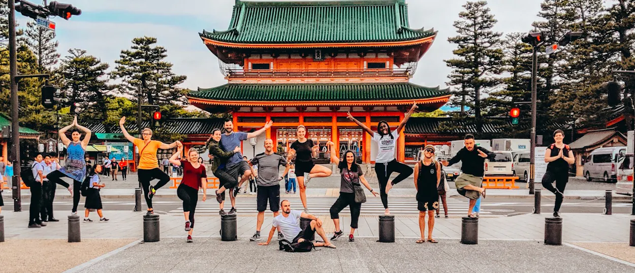Energetic backpackers playfully pose and jump in front of a grand traditional Japanese temple in Osaka.