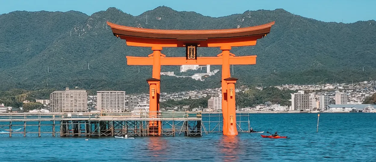 The iconic orange Great Torii Gate of Miyajima Island stands partly submerged in serene blue water.