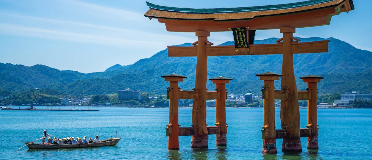 The iconic Great Torii Gate of Miyajima Island stands in the sea, with a boat passing by.