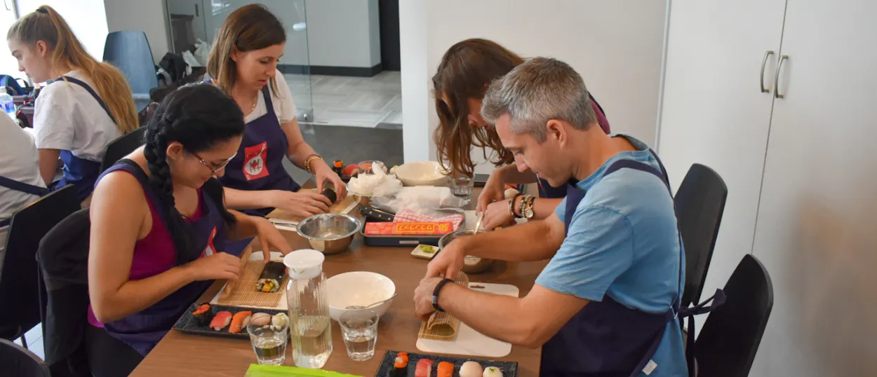 Travelers wearing aprons learn to make sushi rolls during a cooking class in Tokyo, Japan.