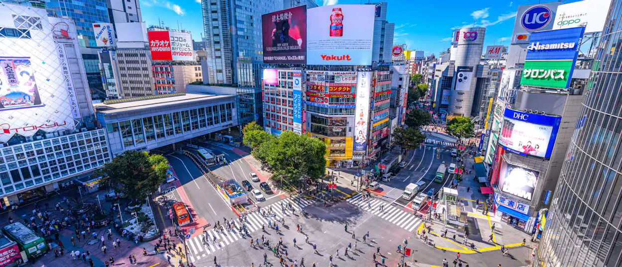 A dynamic aerial view of the iconic Shibuya scramble crossing in Tokyo, bustling with pedestrians.