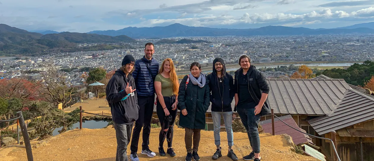 Six happy travelers pose on a mountain overlooking a sprawling city in Hakone, Japan.