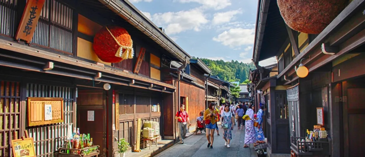 Tourists stroll along a traditional street in Takayama, Japan, lined with historic wooden buildings and shops.