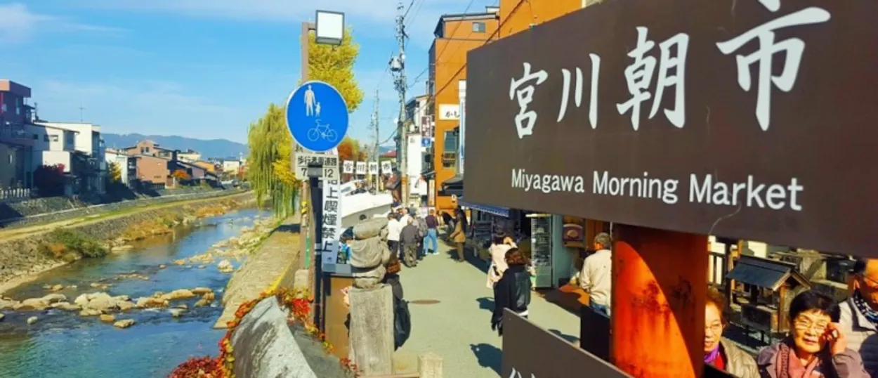 People browse stalls at Miyagawa Morning Market in Takayama on a sunny autumn day.