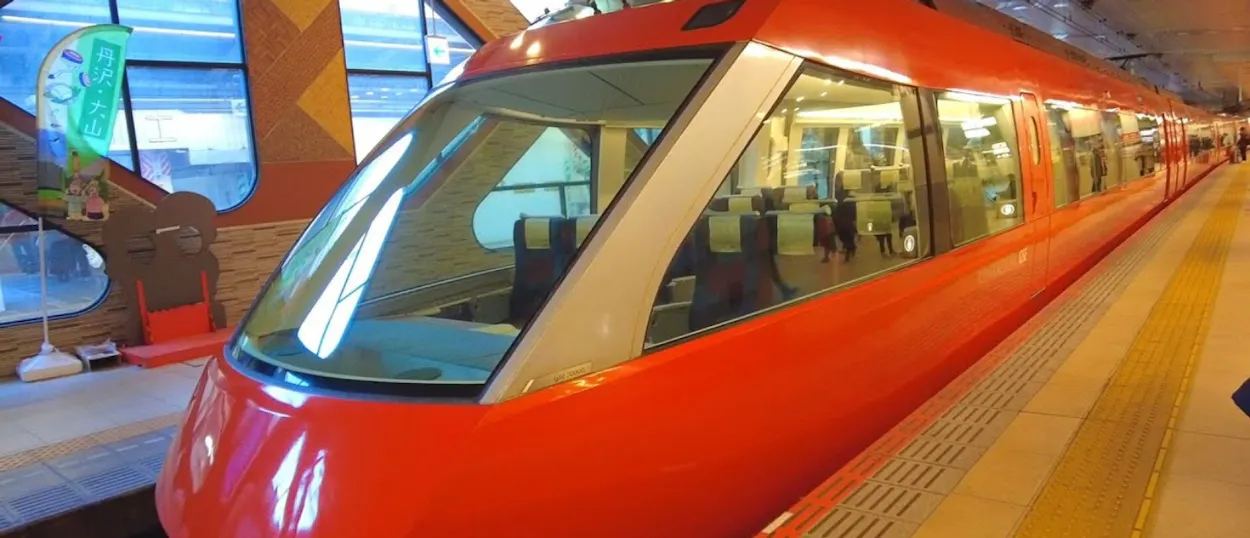 A sleek red modern train with large windows waits at a station platform in Kyoto, Japan.