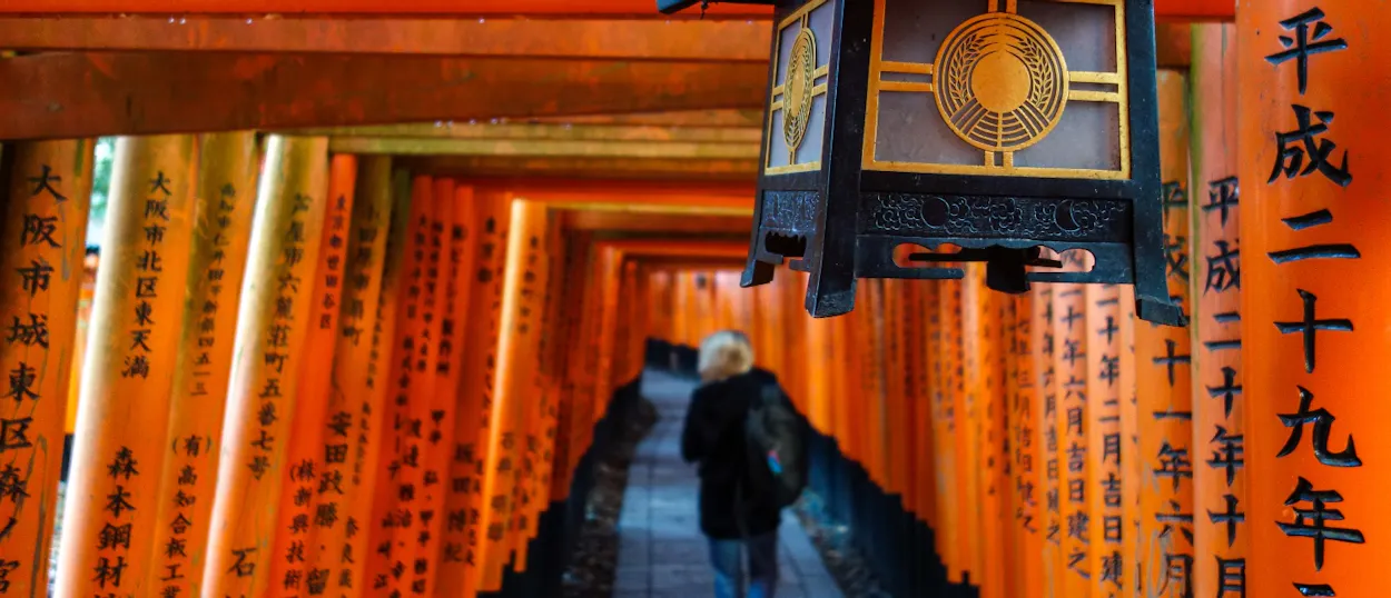 A person walks through endless corridors of vibrant orange torii gates at Fushimi Inari Shrine, Kyoto.
