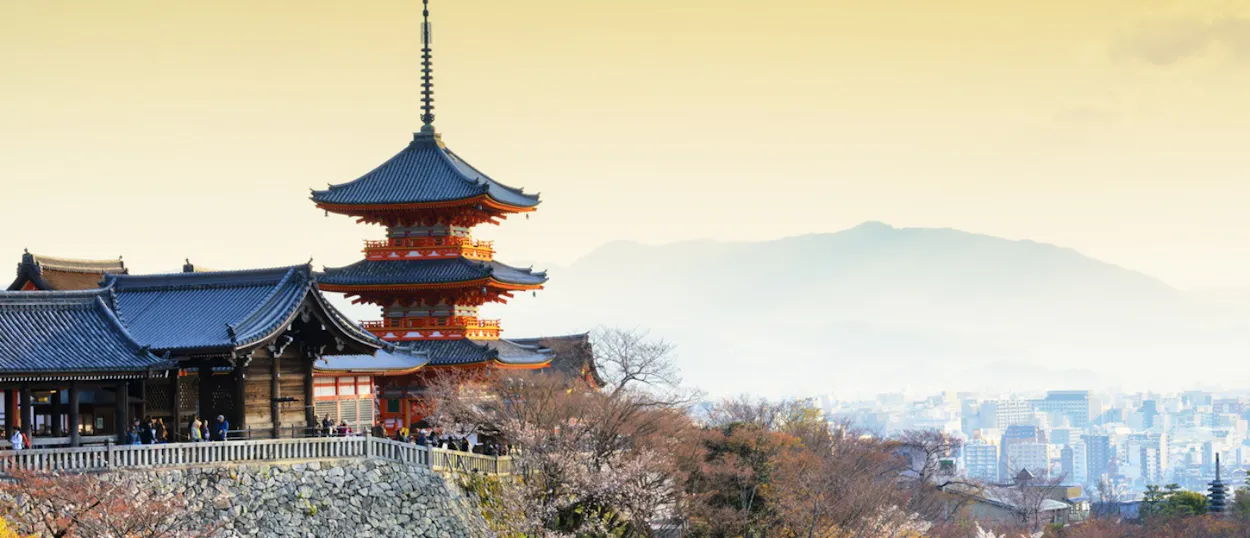 Historic Kiyomizu-dera temple and pagoda overlook Kyoto city and distant mountains under a clear sky.