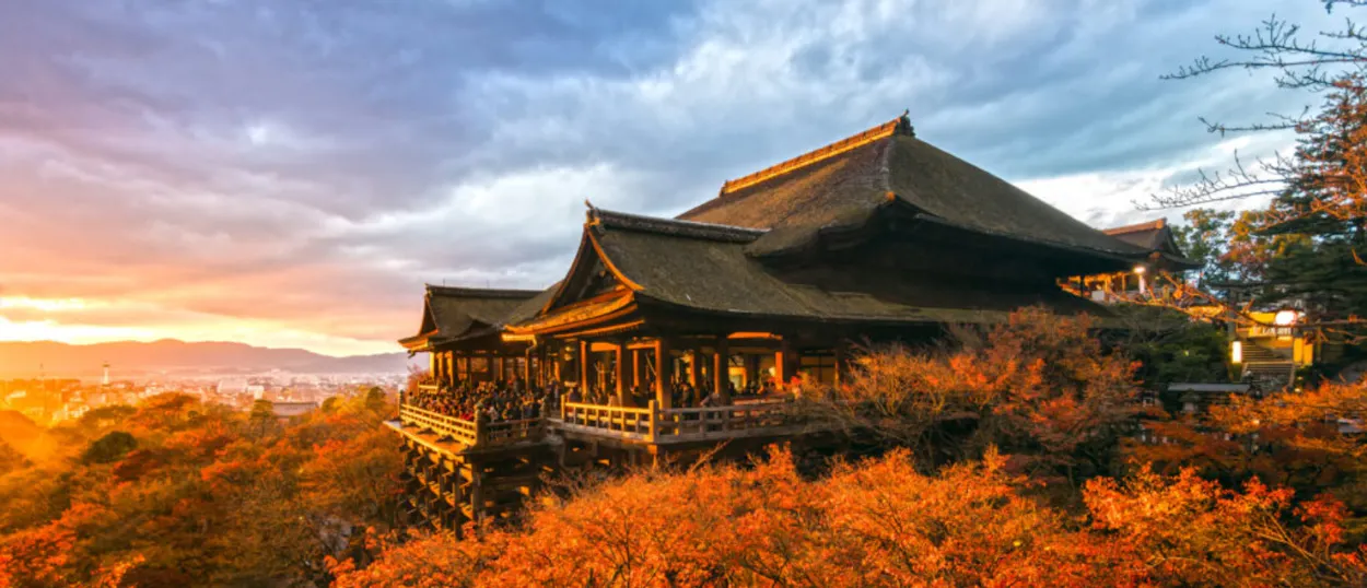 Kiyomizu-dera temple in Kyoto, Japan, glows golden amidst vibrant autumn leaves at sunset.