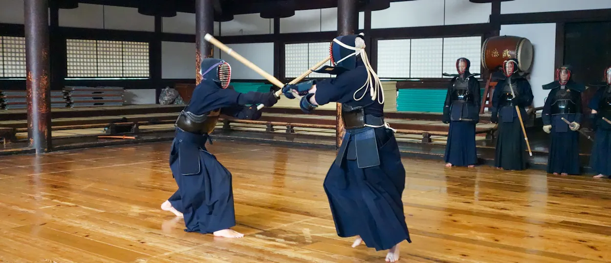 Two people in kendo gear practice with bamboo swords during a traditional class in a Kyoto dojo.