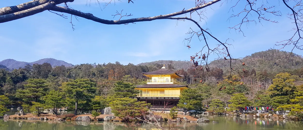 The magnificent Golden Pavilion in Kyoto, Japan, reflected in its serene lake surrounded by lush trees.
