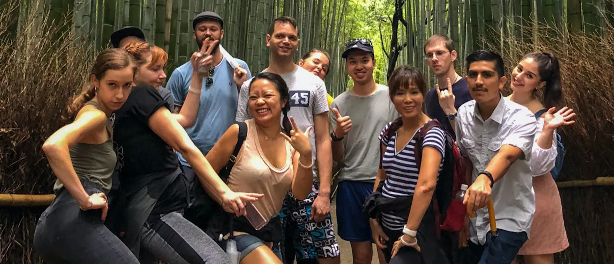 A diverse group of happy backpackers posing playfully in the lush Arashiyama Bamboo Forest, Japan.
