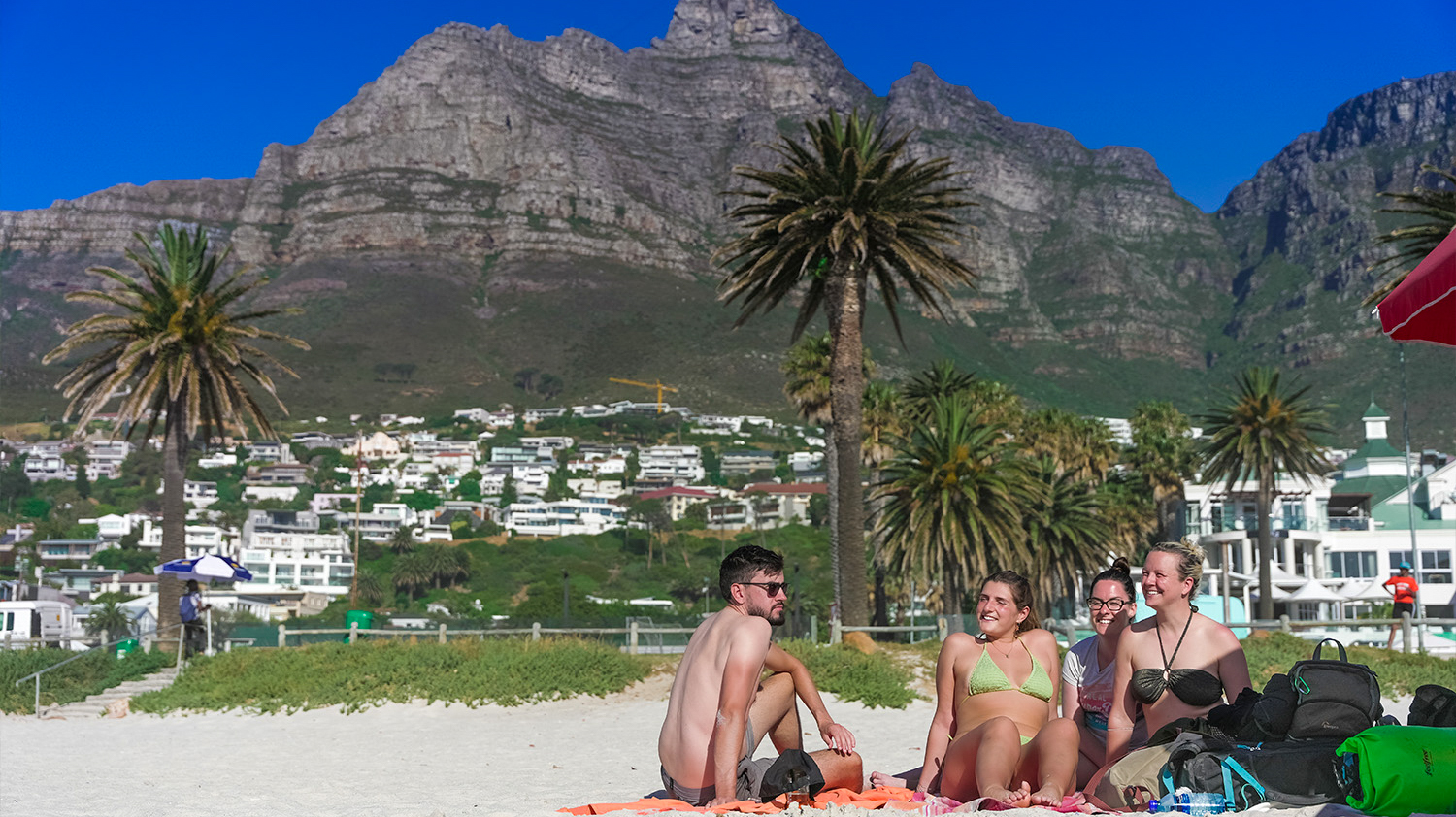 Four happy friends relax on a sunny Cape Peninsula beach with palm trees and Table Mountain.