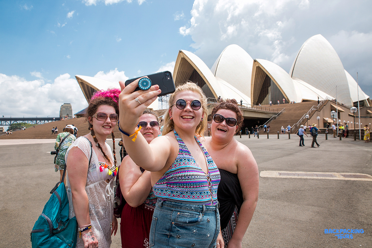 Friends capturing a joyful selfie moment outside the famous Sydney Opera House and Harbour Bridge.