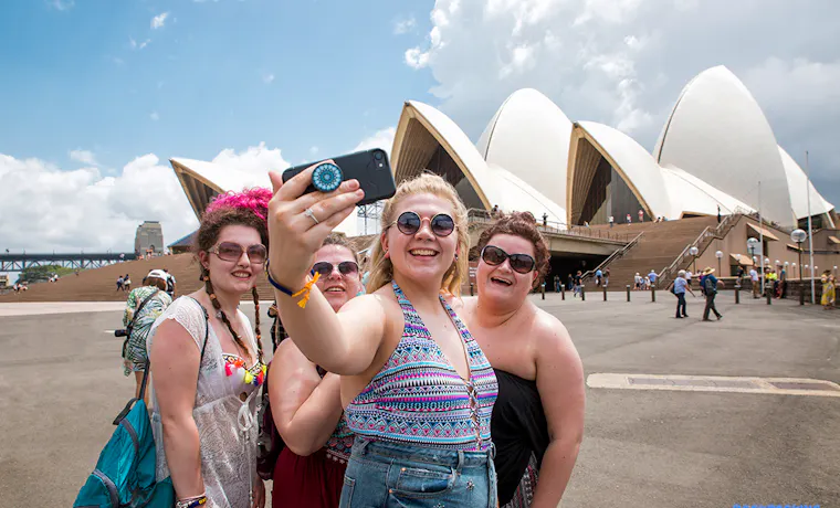 Friends capturing a joyful selfie moment outside the famous Sydney Opera House and Harbour Bridge.