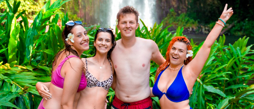 Four happy friends in swimsuits pose in front of Millaa Millaa Falls, Australia.