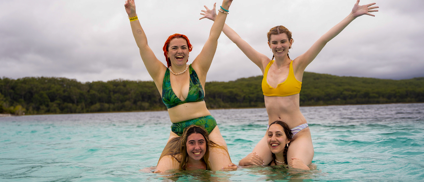 Four happy women on shoulders in the crystal-clear waters of Lake McKenzie, K'gari.