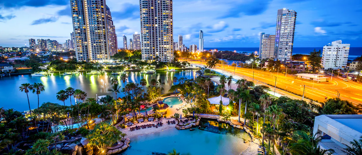 Vibrant Surfers Paradise cityscape at twilight, with illuminated high-rises, resort pools, and ocean views.