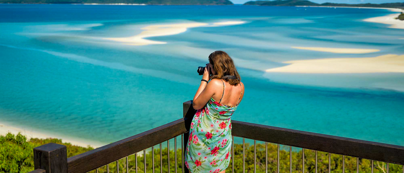 Woman photographs the stunning turquoise waters and white sand swirls of Whitehaven Beach, Whitsundays.