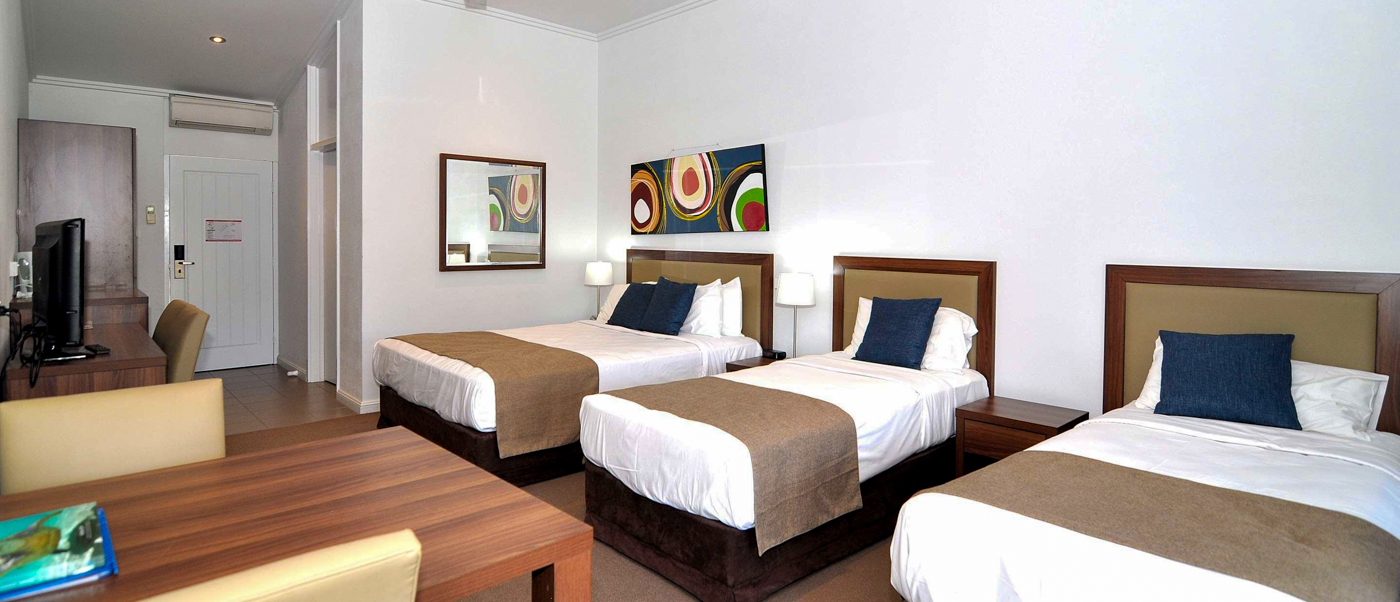 Spacious resort room in Mission Beach with three comfortable beds, a dining table, and TV.