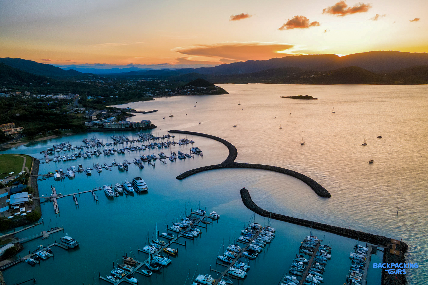 Sunset over the vibrant Airlie Beach marina, filled with boats and surrounded by hills.