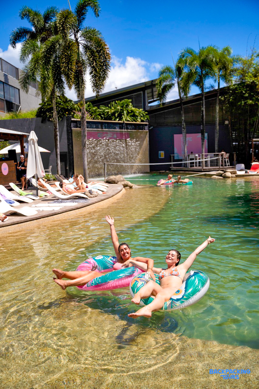 Two happy women relax on colorful floats in a sunny resort pool in Cairns, Australia.