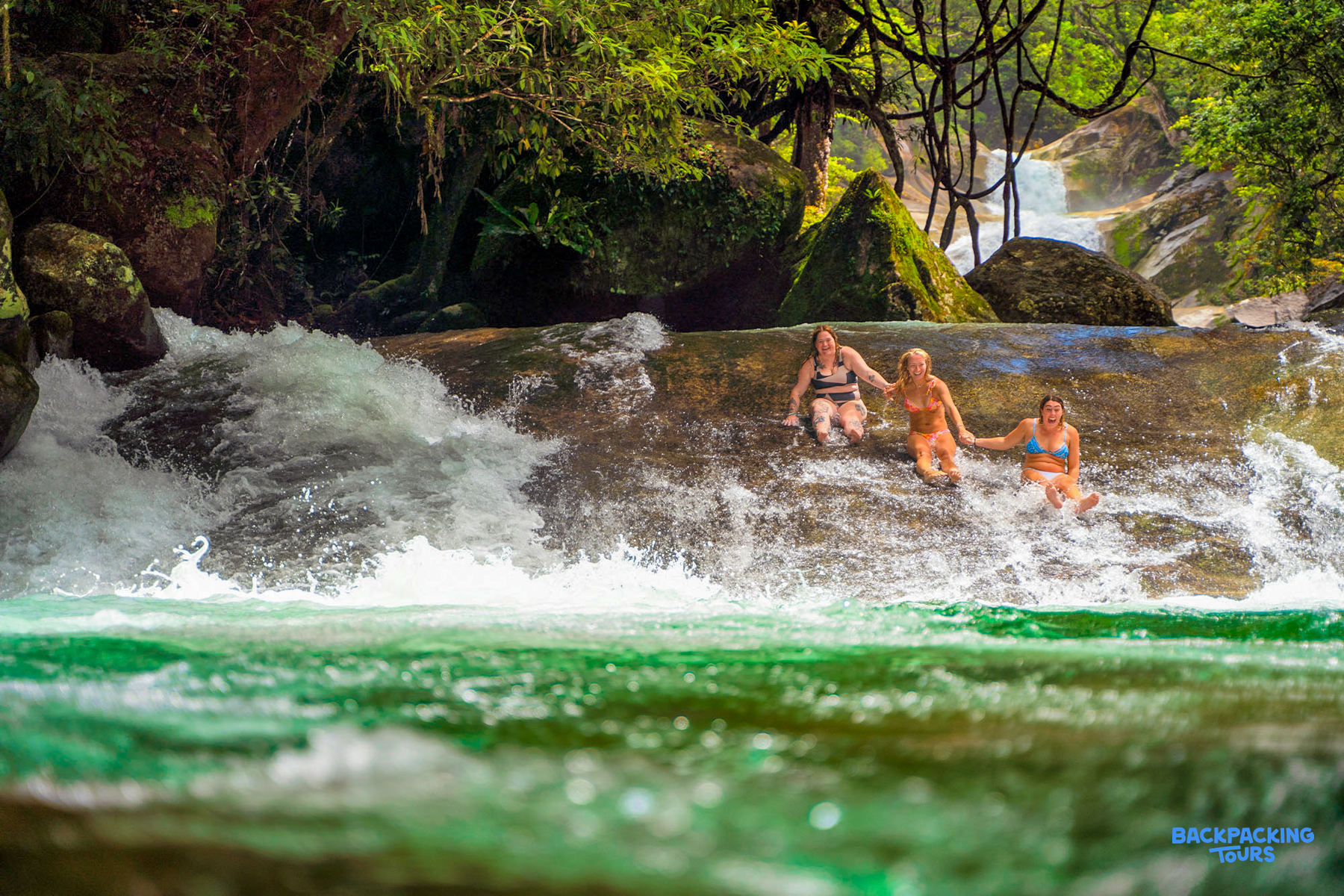 Three women joyfully sliding down Josephine Falls in Australia's lush Atherton Tablelands.