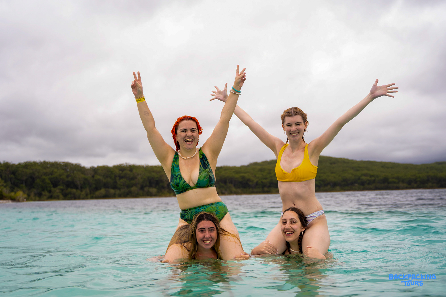 Smiling women on shoulders celebrating in the crystal-clear waters of Lake McKenzie, K'gari.