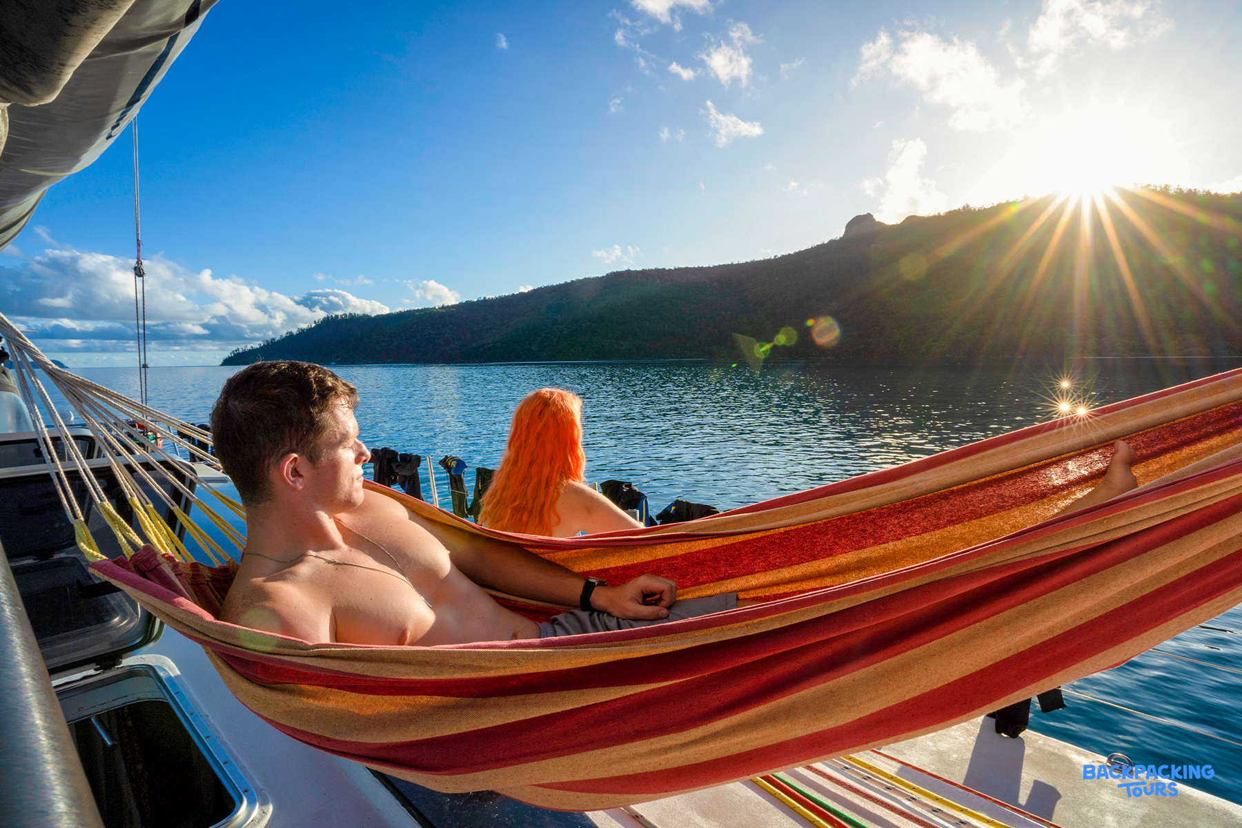 Two people relax in a boat hammock, enjoying the stunning tropical scenery of the Whitsundays.