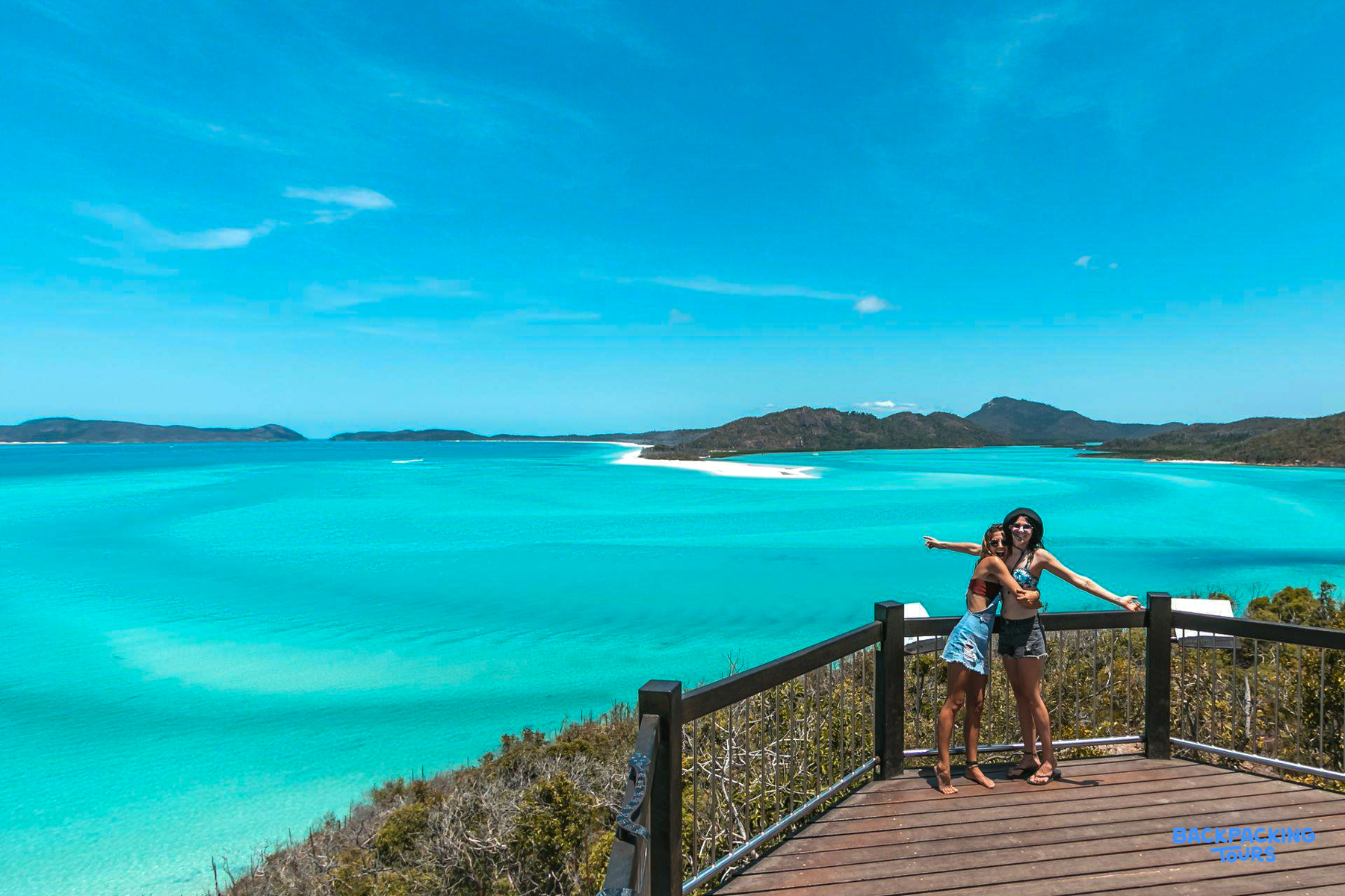 Friends embrace on a scenic deck, overlooking the pristine Whitehaven Beach and Whitsundays islands.