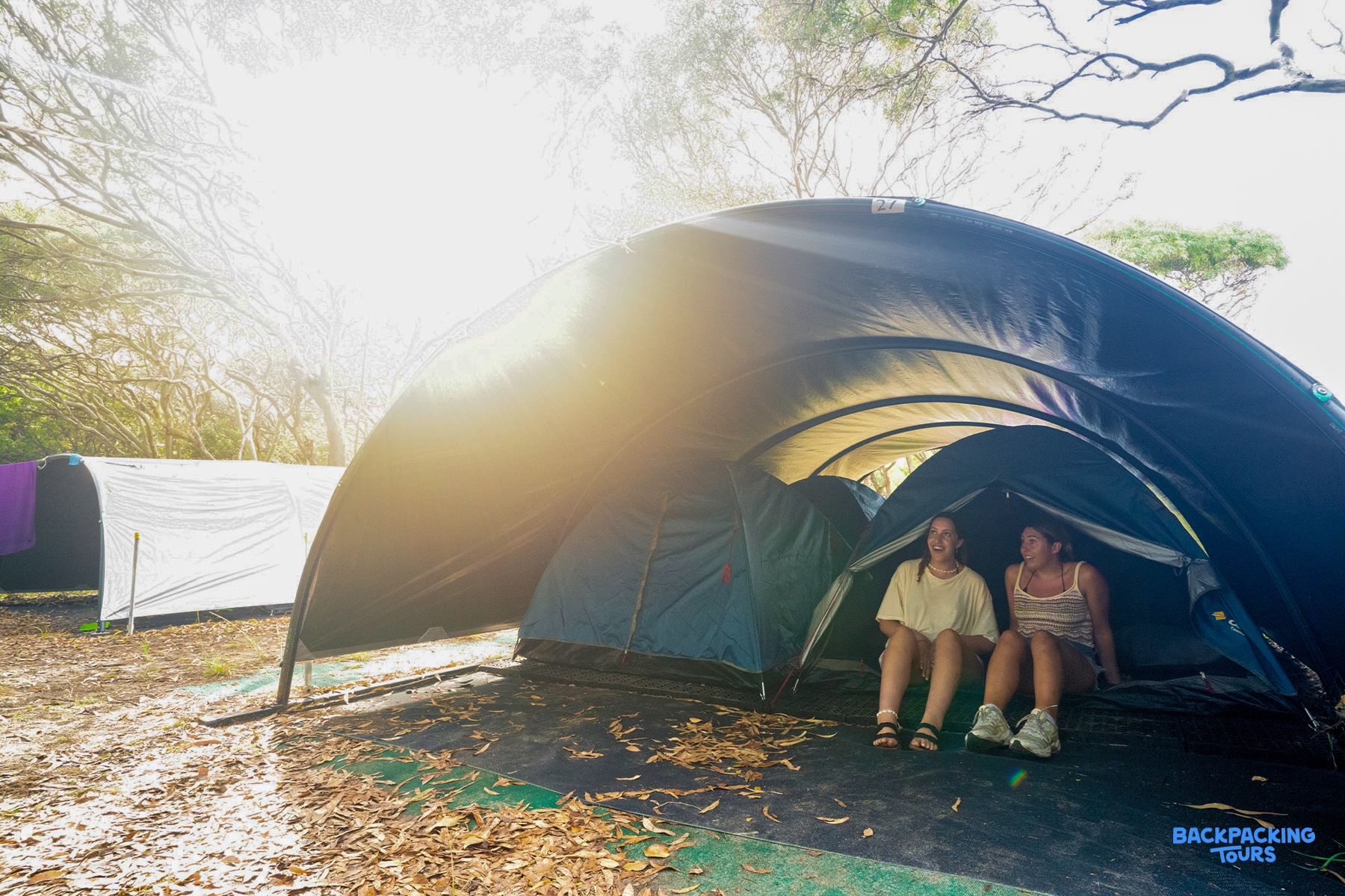 Two friends relaxing inside their tent at a sunny K'gari island campsite.