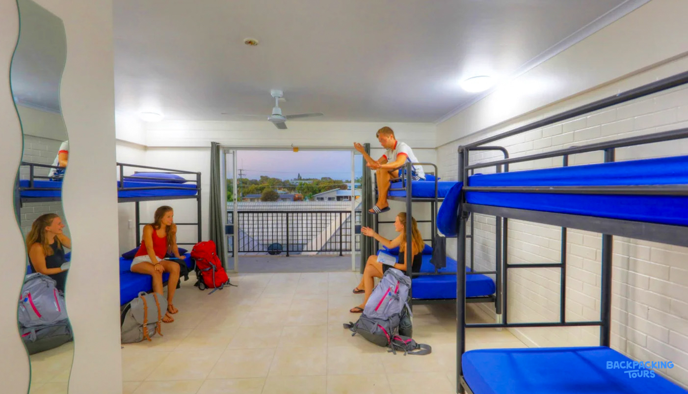 Four backpackers relax in a bright hostel dorm room at Rainbow Beach, Australia.