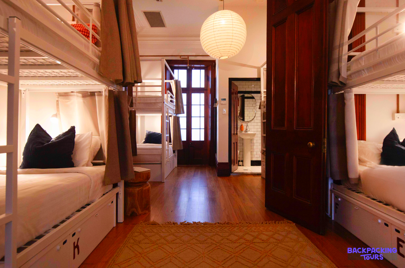 A bright and welcoming hostel dorm room in Sydney featuring comfortable bunk beds with privacy curtains.