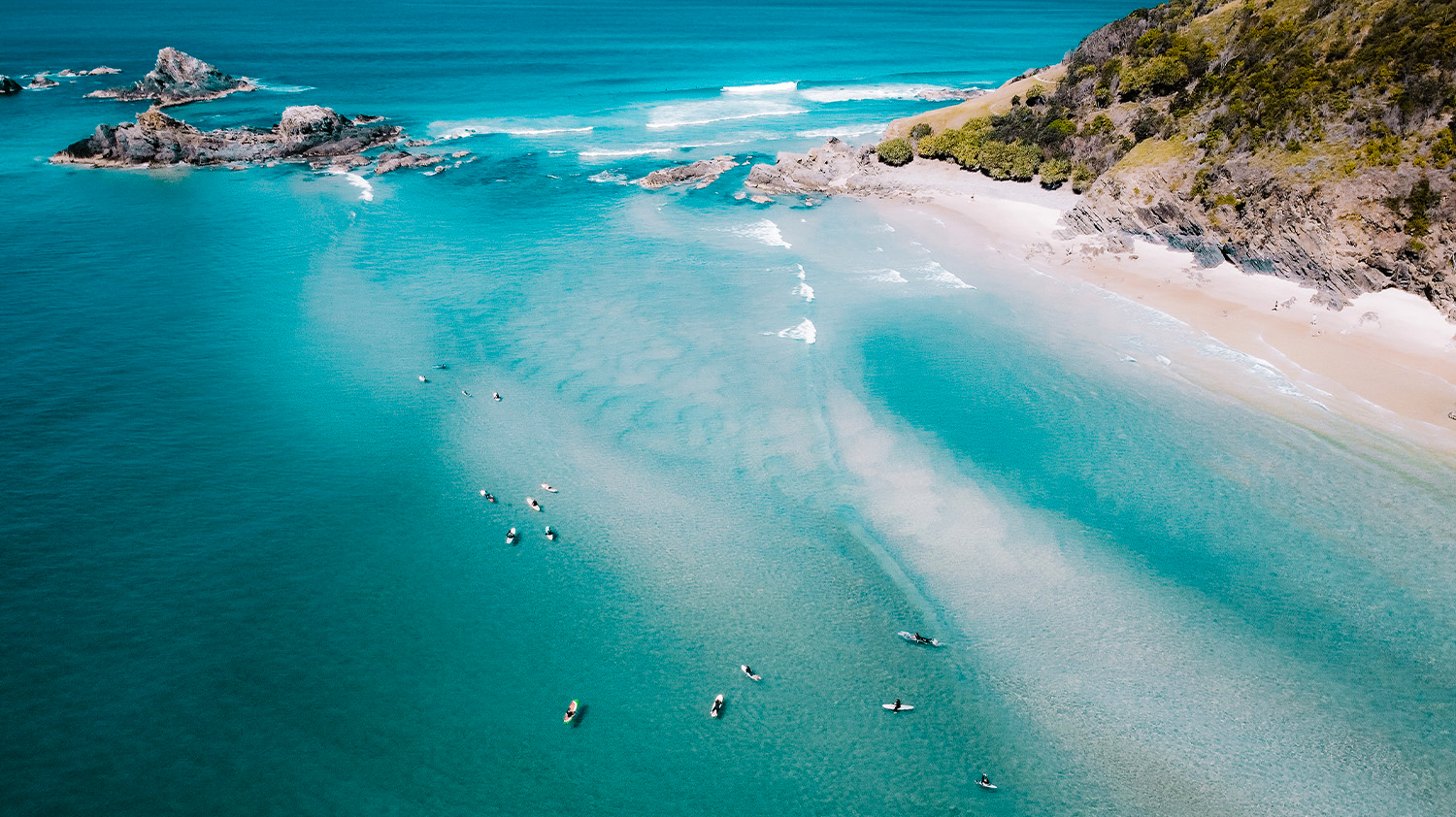 Aerial view of surfers paddling in the clear turquoise waters off Byron Bay beach.