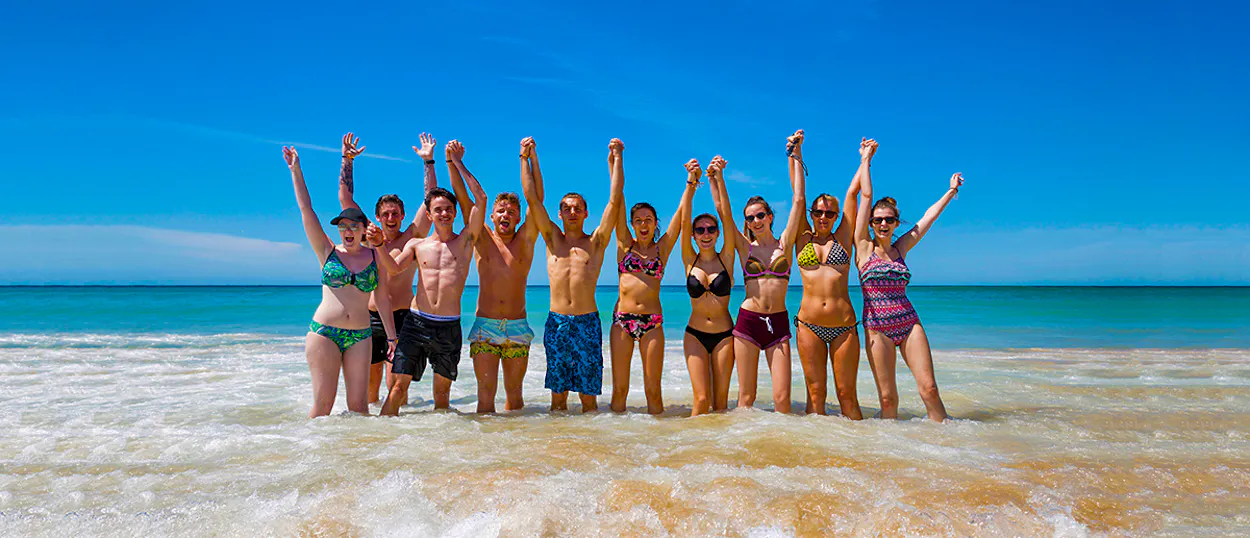 A happy group of young travelers raising their arms in the clear blue water at Bondi Beach.