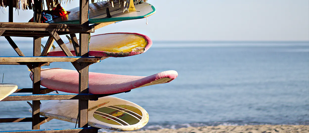 Colorful surfboards stacked on a wooden rack on the sandy beach at Byron Bay, Australia, with the ocean in the background.