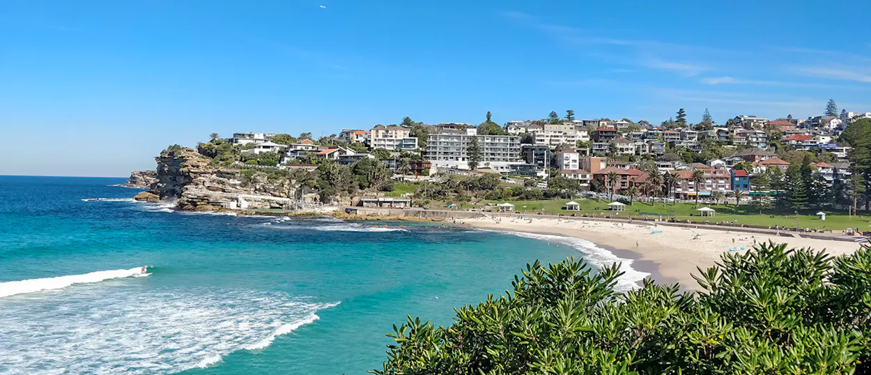 Beautiful Coogee Beach in Sydney, Australia, with clear blue water, a sandy shore, and coastal homes.