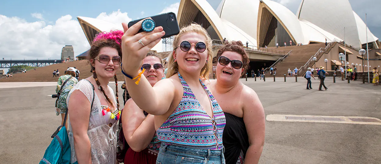 Smiling women take a selfie with the Sydney Opera House and Harbour Bridge in the background.