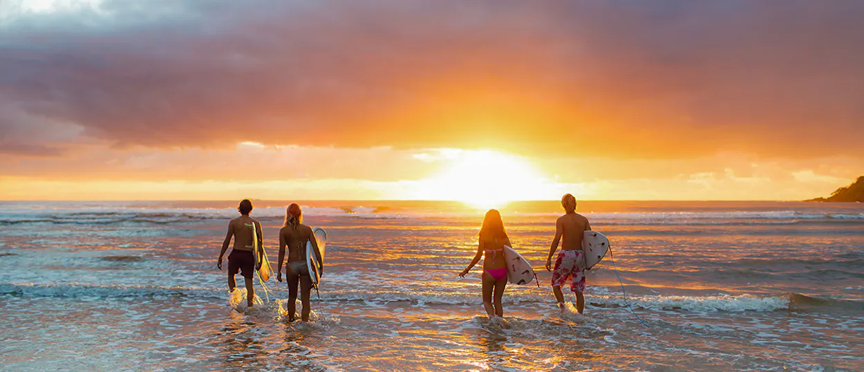 Backpackers with surfboards wade into the sparkling ocean water at sunset in Byron Bay.