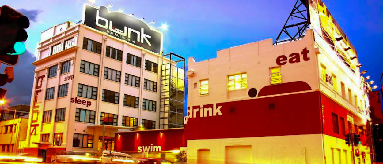 Vibrant Bunk Hostel building and an adjacent building with 'eat' and 'drink' signs in Brisbane.
