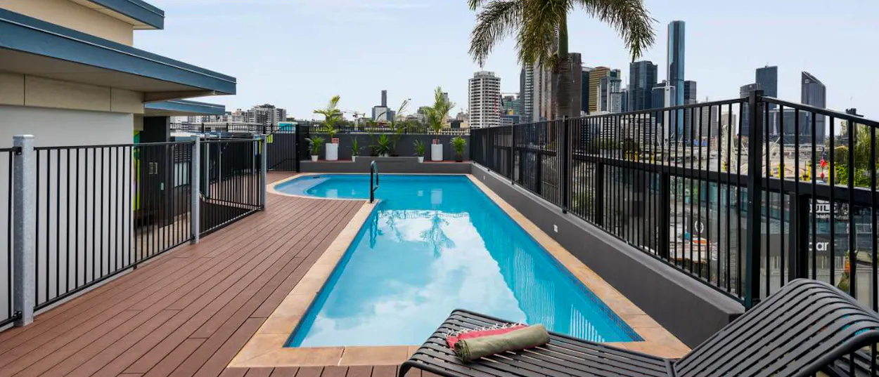 Two sparkling blue rooftop pools on a wooden deck overlooking the Brisbane city skyline.