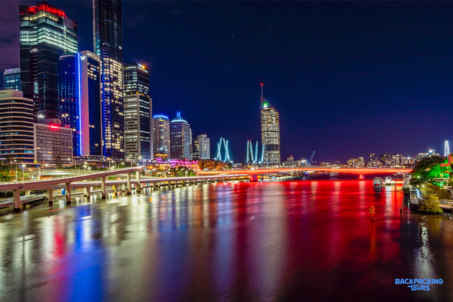 Vibrant Brisbane city skyline at night, with colorful lights reflecting on the calm river.