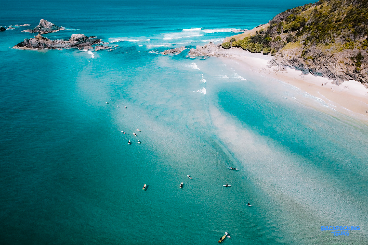Surfers and paddleboarders enjoy the clear turquoise waters and scenic rocky coastline of Byron Bay.