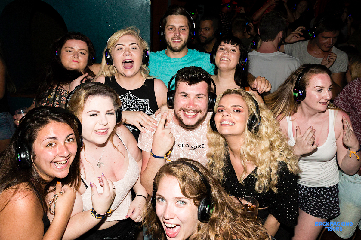 A group of happy young backpackers smiling and laughing at a lively silent disco party in Sydney.