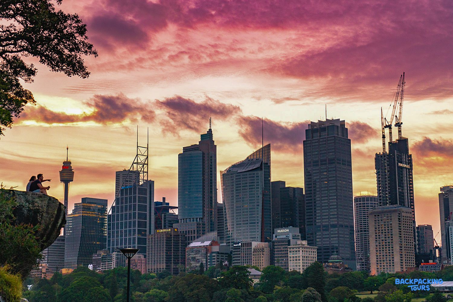 Two people watch a breathtaking pink and orange sunset over the Sydney city skyline.