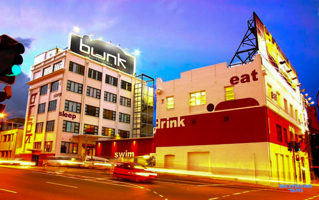 Bunk Hostel in Brisbane at dusk, with bright signs for sleep, swim, eat, and drink.