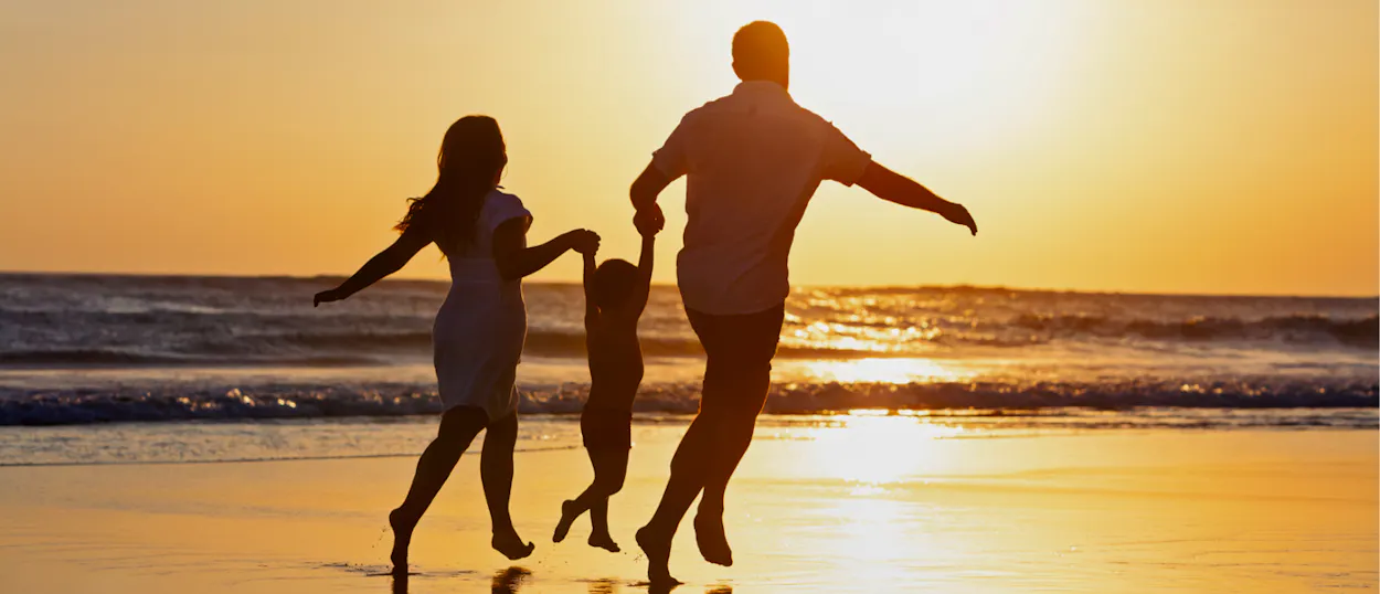 Happy family silhouetted against a vibrant sunset, running barefoot on Seminyak beach.
