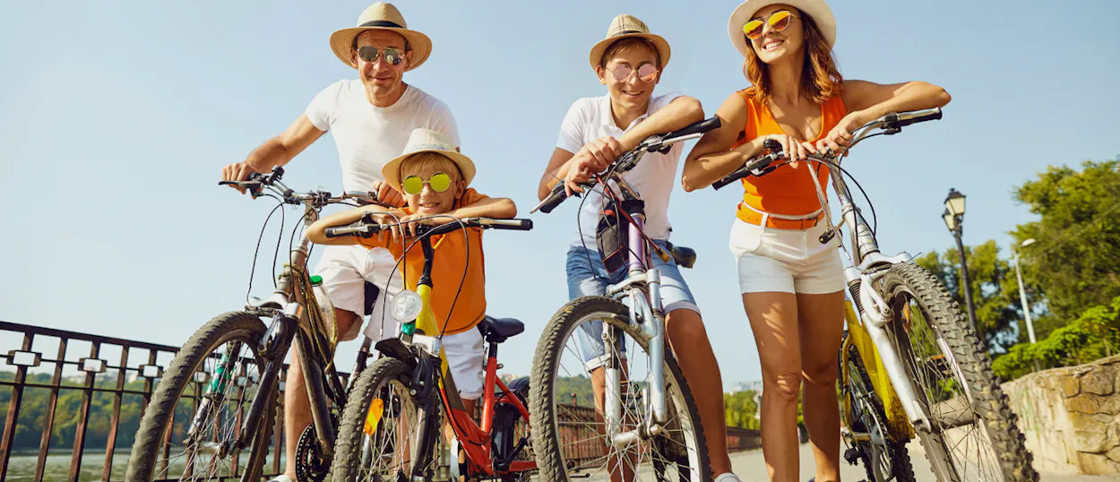A happy family of four wearing hats and sunglasses, posing with their bicycles on Gili Trawangan.