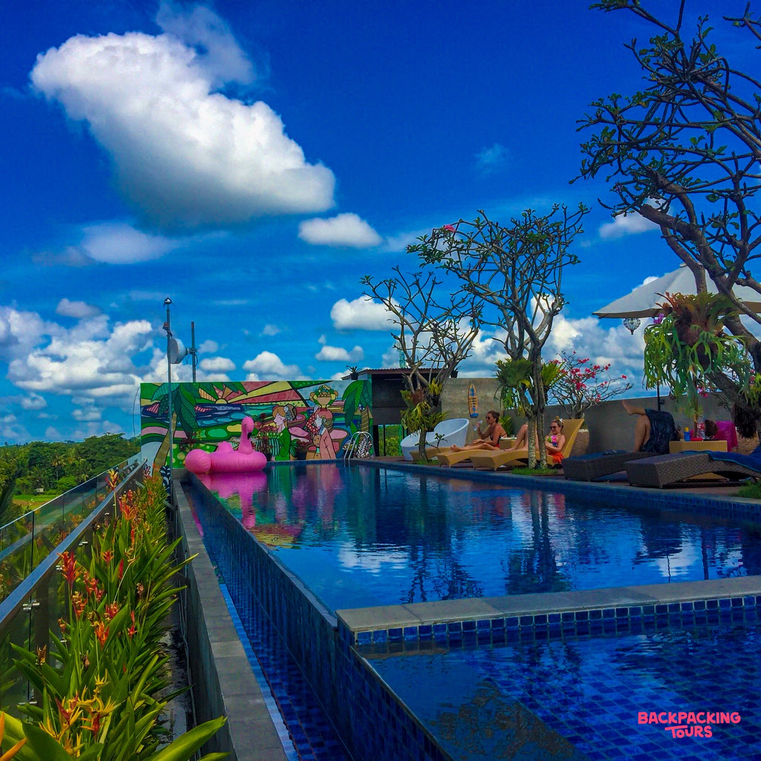 Guests enjoy a vibrant rooftop swimming pool in Ubud, featuring a pink flamingo float and lush views.
