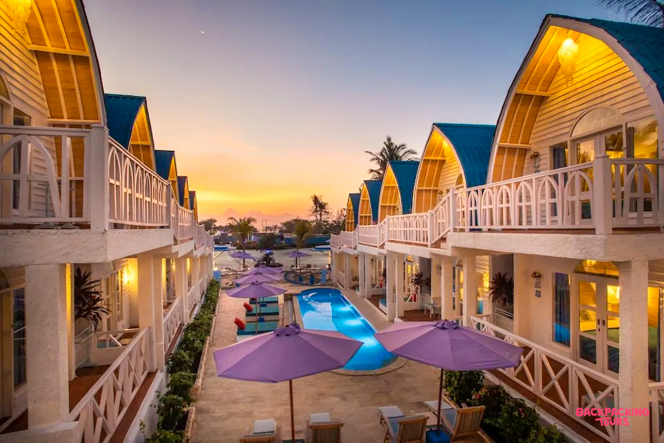 Tropical resort bungalows with blue roofs and a pool glow under a vibrant Gili Trawangan sunset.