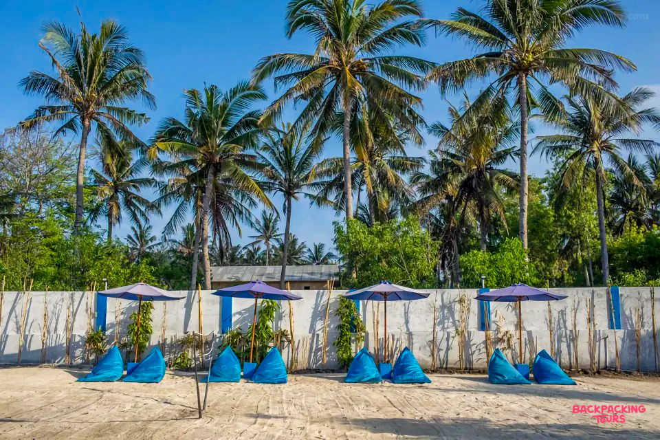 Relaxing blue bean bags and umbrellas on a sandy beach under tall palm trees in Gili Trawangan.